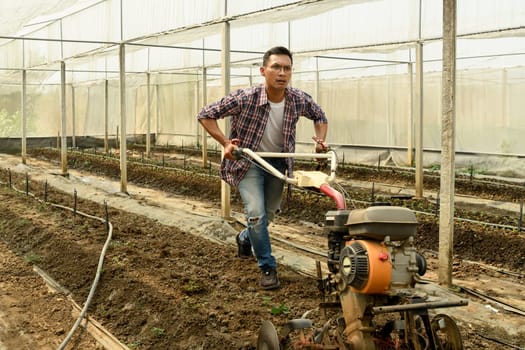 Farmer tilling soil in a greenhouse preparing the land for planting.