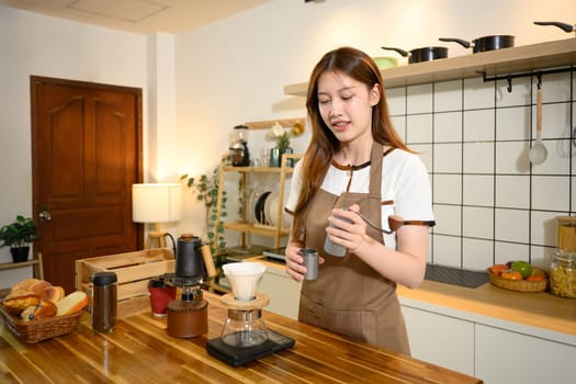 Young woman in apron preparing pour over coffee in a cozy home kitchen.