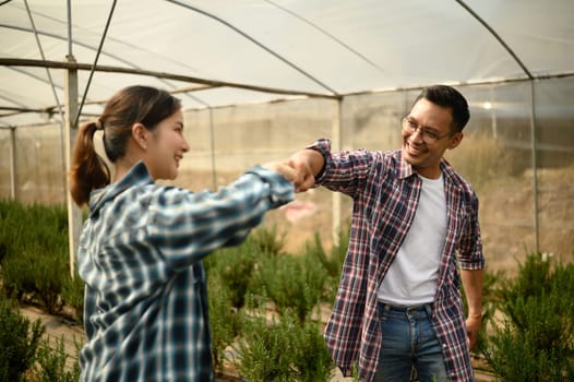 Happy asian farmers sharing a fist bump in a greenhouse farm.