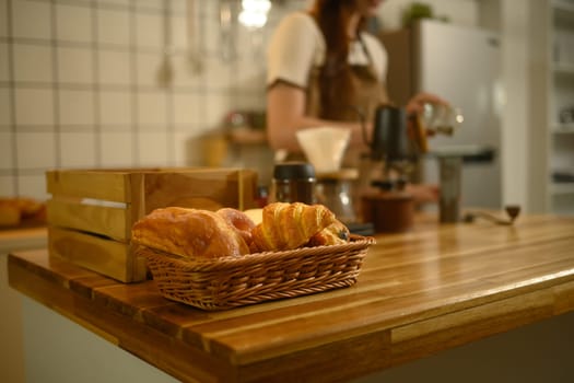 Close up of fresh croissants in a wicker basket on wooden kitchen counter.