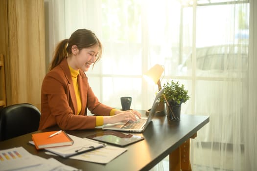 Smiling young entrepreneur working at a home office desk with laptop and documents.
