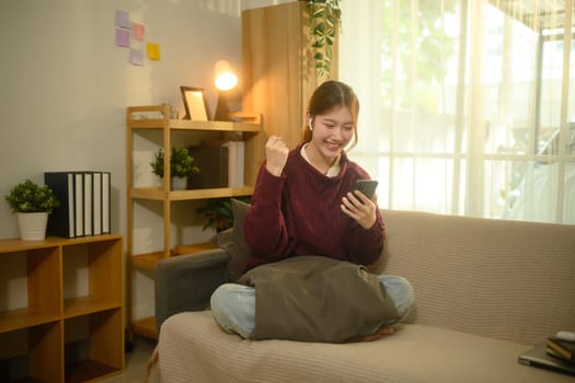 Cheerful young woman celebrating good news while looking at her smartphone.