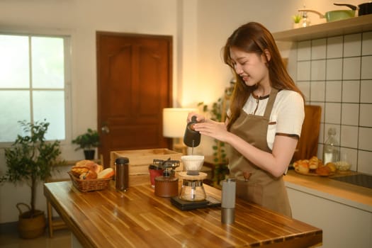 Smiling young woman preparing fresh coffee in a cozy home kitchen.