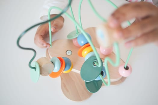 Young child plays with a colorful wooden bead maze on a table.