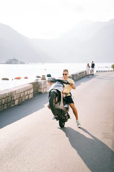 Smiling young man lifted a motor scooter onto the rear wheel while sitting on the seat. High quality photo