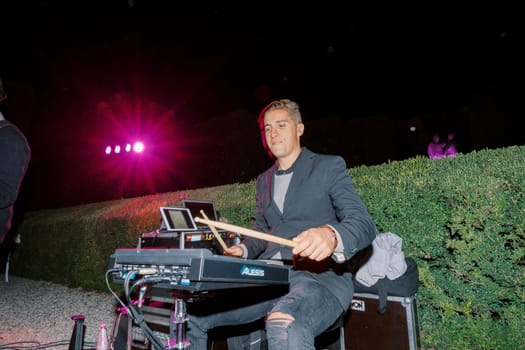 Drummer with sticks sitting at a modern electronic drum kit in the garden. High quality photo
