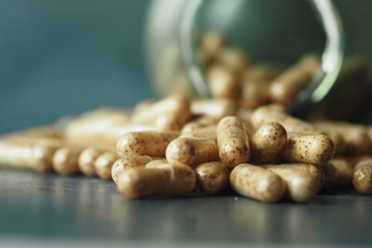 Herbal capsules are spilled from a glass jar onto a smooth surface.