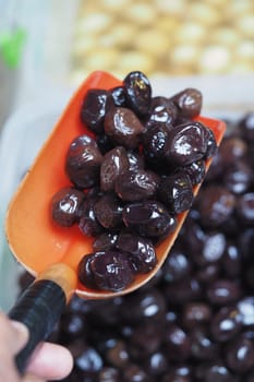 A vendor scoops shiny black olives with a shovel at a local market.