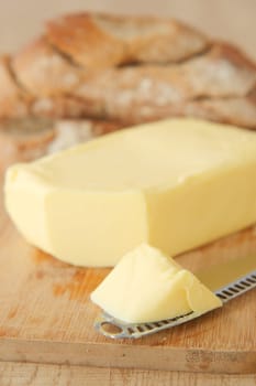 Fresh butter sits next to a loaf of crusty bread on a cutting board.