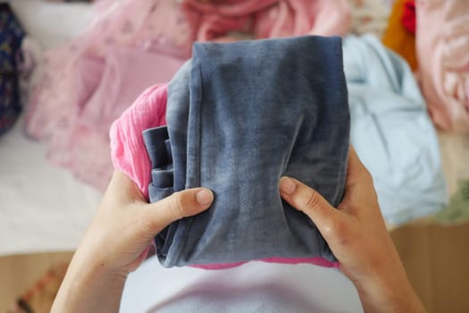 Hands hold neatly folded clothes while organizing a bedroom space.