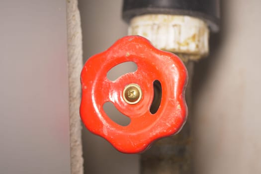 A red valve handle is positioned on a pipe for plumbing adjustments.