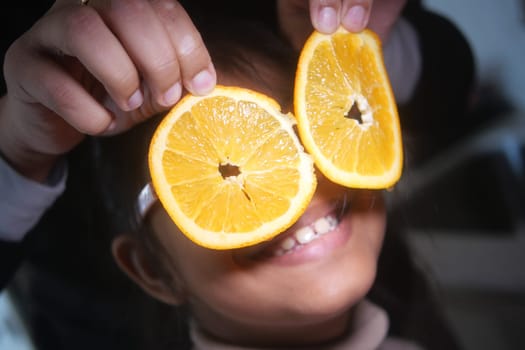Young girl enjoys playfully holding orange slices in front of her face, smiling.