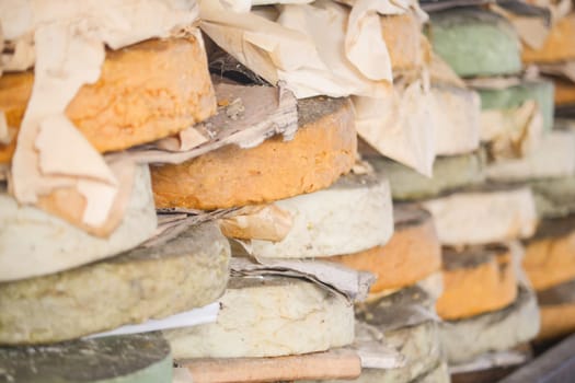 Cheese wheels of various colors are stacked in a traditional cellar, aging.