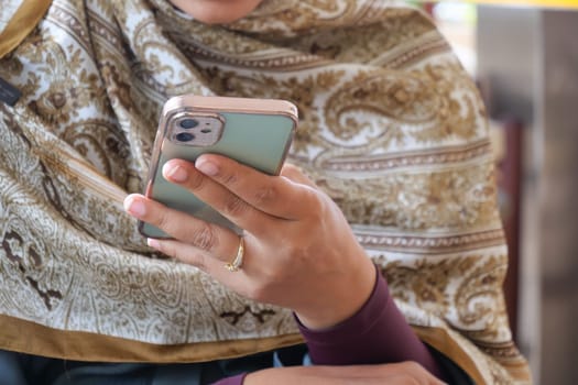 Woman with scarf is focused on smartphone in busy market.