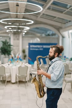 Saxophonist plays the saxophone in a restaurant near the set tables. High quality photo