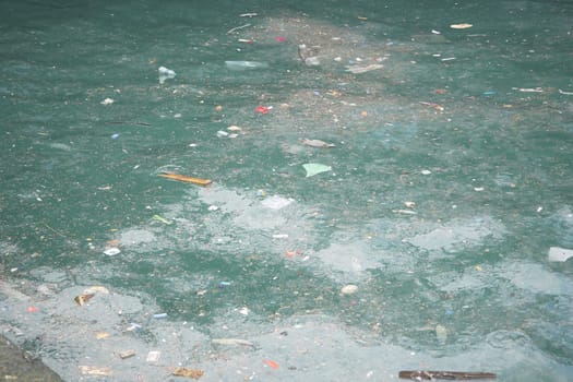 Trash and debris accumulate on the surface of water in a city.