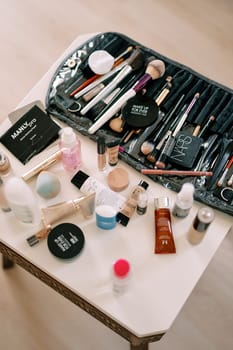 Table with a set of makeup brushes and various cosmetics stands in the room. High quality photo