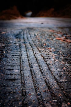 The image captures distinct tire tracks on a gravel road, symbolizing adventure, exploration, and the journey into nature amidst a rugged, earthy environment.