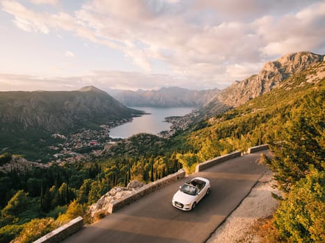 Bride and groom are driving in a white convertible along a road in the mountains above the Bay of Kotor. Montenegro. Drone. High quality photo