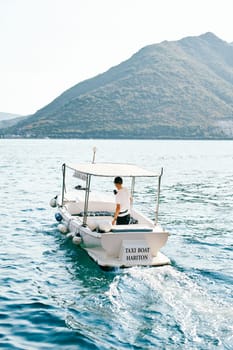 White boat with a canopy floats on the sea. Caption: Taxi boat Hariton. High quality photo