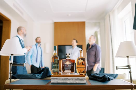 Three bottles of expensive whiskey stand on the table against the backdrop of laughing men. High quality photo