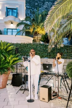 Male musical group sings on a paved area near a restaurant. High quality photo