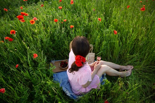 A young woman enjoys a picnic amidst a vibrant poppy field, savoring rose wine and fresh berries.