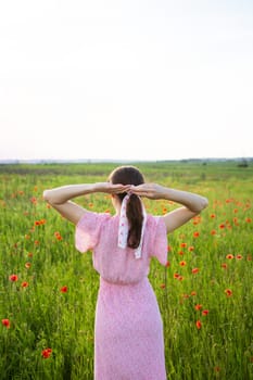 A woman in a pink floral dress enjoys a serene moment in a poppy field, her hair tied up in a silk ribbon.