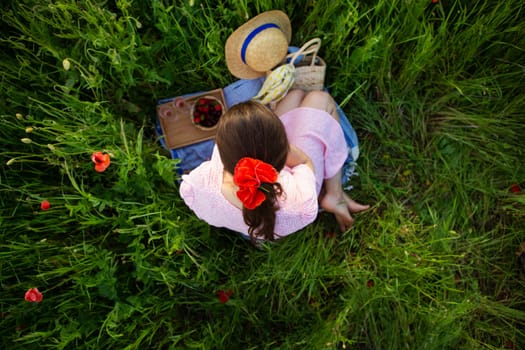 A young woman enjoys a tranquil picnic amidst a vibrant poppy field, surrounded by nature's beauty.