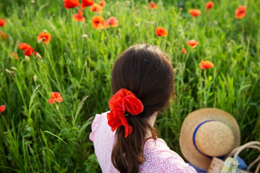 A woman sits in a poppy field, adorned with poppy flowers in her hair, enjoying the summer scenery.