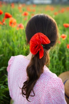 A woman with a red poppy in her hair, stands in a field of poppies, enjoying the summer scenery.