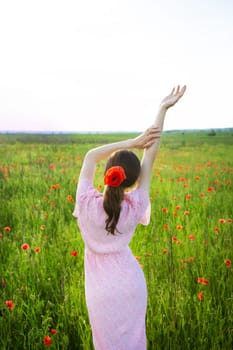 A woman in a pink dress with a red poppy in her hair enjoys a summer day in a poppy field.