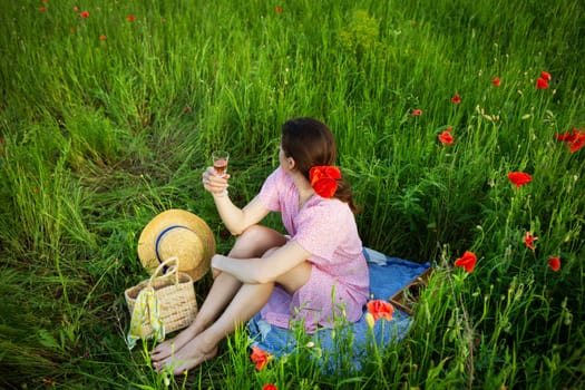 A woman enjoys a picnic in a vibrant poppy field, raising a glass of rose wine.