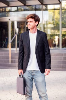 young adult man in casual suit standing holding a briefcase in front of an office building, concept of entrepreneur and business