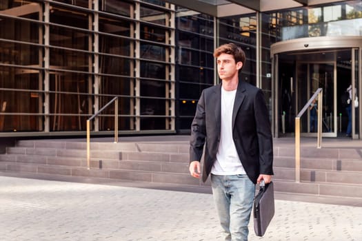 young adult man in casual suit walking in front of an office building holding a briefcase, concept of entrepreneur and business, copyspace for text