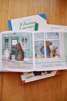 Open book of fairy tales about the beaver workshop lies on a stack of books on a wooden table. High quality photo
