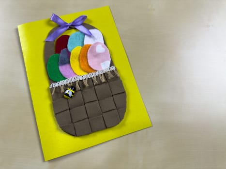 Cheerful handmade Easter card features woven basket filled with vibrant felt eggs and cute bee. It's wonderful way to share festive greetings and celebrate the joy of Easter with friends and family