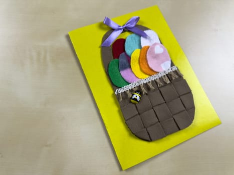Vibrant handmade Easter card showcases woven basket filled with assorted felt eggs and charming bee. Perfect for sending heartfelt wishes and celebrating joyful spirit of Easter with loved ones