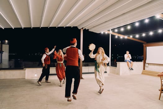 Group of men and women in national costumes dance with a tambourine on stage. High quality photo