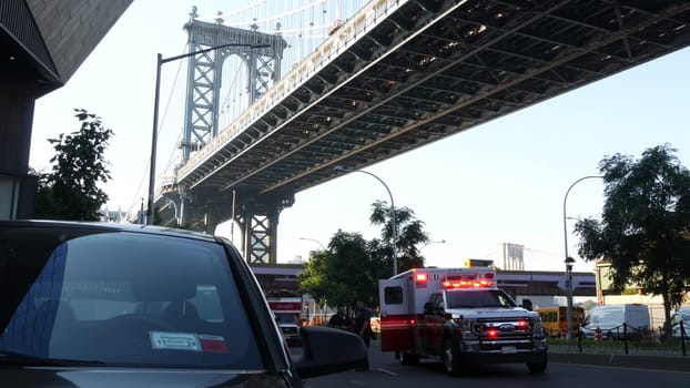 New York City, United States - 7 Sept 2023: NYFD Ambulance medical emergency, American fire department paramedic truck siren under Manhattan bridge. USA 911 red vehicle on street. NYC first responders