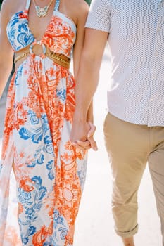 Man and woman walk holding hands along the road. Cropped. Faceless. High quality photo