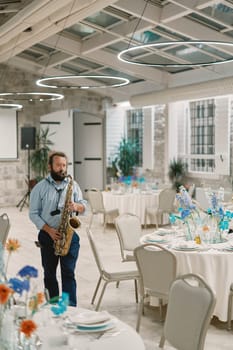 Saxophonist plays the saxophone near festive tables in a restaurant. High quality photo