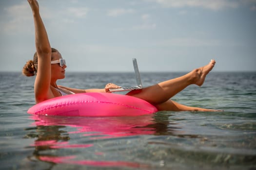 A woman is floating on a pink inflatable raft in the ocean while using a laptop. Concept of relaxation and leisure, as the woman enjoys her time in the water while working on her laptop