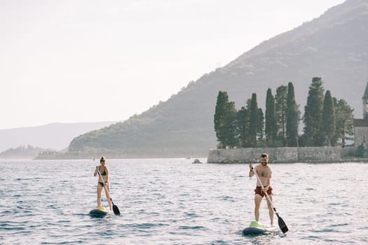 SUP surfers float on boards using oars along the Bay of Kotor. Montenegro. High quality photo