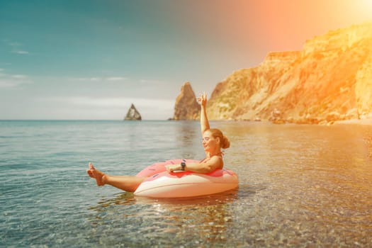 Woman laptop sea. Freelancer woman in sunglases floating on an inflatable big pink donut with a laptop in the sea. People summer vacation rest lifestyle concept