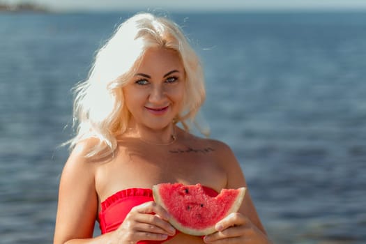 Blonde woman in red bikini holds a juicy watermelon slice near the ocean. Summer vibes.