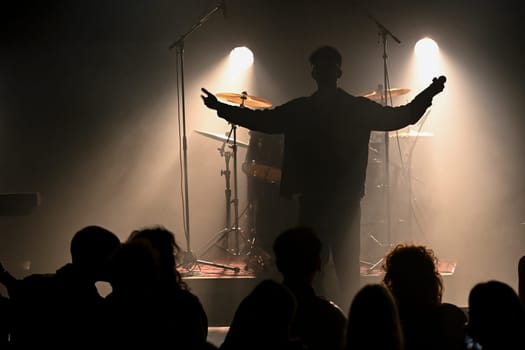 An exhilarating concert unfolds as a charismatic musician captivates the audience with an expressive performance illuminated by dramatic stage lights, creating a vibrant atmosphere.