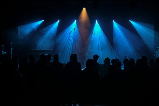 Musician stands center stage surrounded by blue lighting, creating a vibrant atmosphere. The audience watches intently, enjoying the live musical experience.