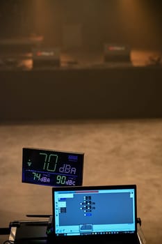 Sound level is monitored at a concert, showing 70 dBA on a digital display. A laptop runs software for tracking decibel levels as part of audio management.