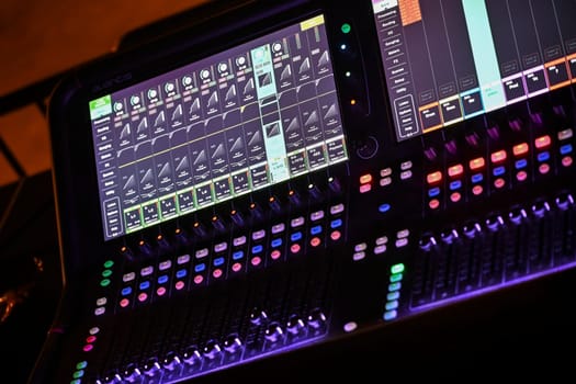 Focused sound engineer adjusts sliders and knobs on a digital mixing console while preparing for a performance in a lively venue atmosphere.